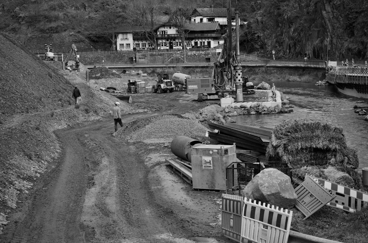 Monochrome image of construction site next to a river with heavy machinery and workers.